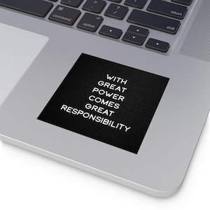 Può includere: Un adesivo nero con la scritta bianca "WITH GREAT POWER COMES GREAT RESPONSIBILITY", posto su un laptop argentato. L'adesivo è rettangolare e il testo è allineato verticalmente.