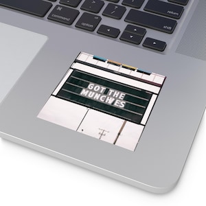 以下が含まれることがあります： 「GOT THE MUNCHIES」の文字が白抜きで書かれた黒い背景のステッカー。ステッカーは長方形で白い縁取りがある。背景には電柱のある街並みが描かれている。