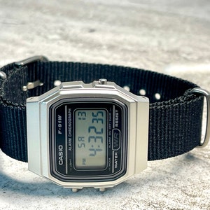 Pu&ograve; includere: Un orologio digitale Casio F-91W argentato con un cinturino in nylon nero. Il quadrante dell'orologio mostra l'ora, la data e le impostazioni della sveglia. L'orologio &egrave; resistente all'acqua.