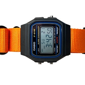 May include: A black Casio F-91W digital watch with an orange nylon strap. The watch face displays the time, date, and alarm settings. The watch is water resistant.