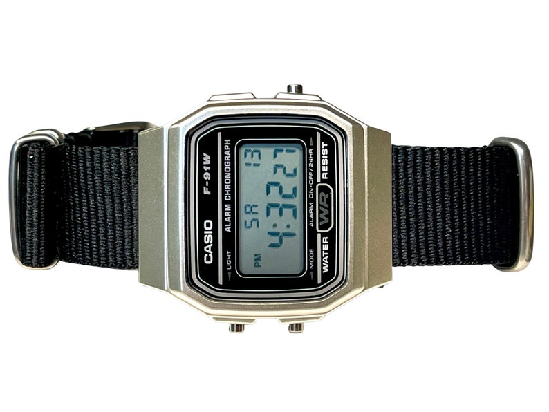 Pu&ograve; includere: Un orologio digitale Casio F-91W argentato con un cinturino in nylon nero. Il quadrante dell'orologio mostra l'ora, la data e le impostazioni della sveglia. L'orologio &egrave; resistente all'acqua.