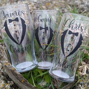 May include: Three clear glass pint glasses with black tuxedo designs and personalized names: James Groom, Gary Best Man, and Chris Usher.