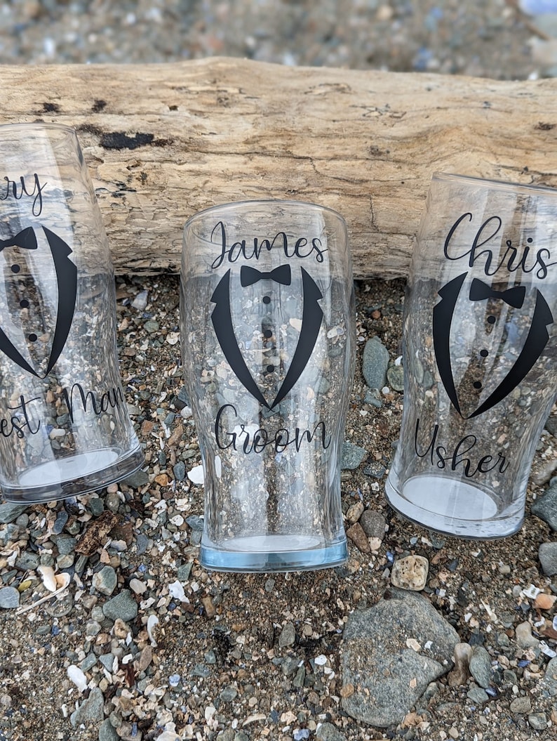 May include: Three clear glass beer mugs with black tuxedo designs and text. The mugs read "James Groom", "Chris Usher", and "Best Man".