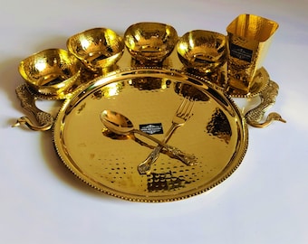 May include: A gold-toned serving set with a large round plate, four small bowls, a tall cup, a fork, and a spoon. The plate and bowls have a hammered texture and the handles of the plate are shaped like swans.