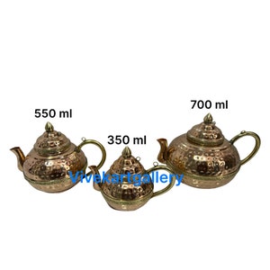 Può includere: Tre teiere in rame con superfici martellate e dettagli dorati. Le teiere sono etichettate con 350 ml, 550 ml e 700 ml.