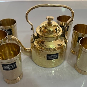 May include: A set of six gold-toned metal teacups and a hammered gold-toned metal teapot with a handle. The teapot and cups have a hammered texture and a black sticker with the text "Viver Art Gallery".