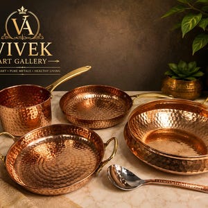 Puede incluir: Juego de utensilios de cocina de cobre con texturas martilladas y asas de latón. El conjunto incluye una cacerola, sartenes y una fuente para servir. El logotipo de Vivek Art Gallery es visible.