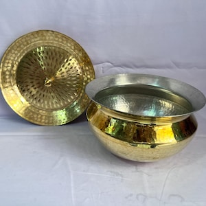 May include: A hammered brass pot with a lid. The pot has a silver interior and a rounded shape. The lid is also hammered brass and has a small knob on top.
