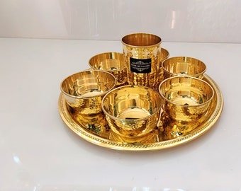 May include: A gold-toned serving set with a hammered finish. The set includes a large round tray with a beaded edge, six small bowls, and a tall tumbler.
