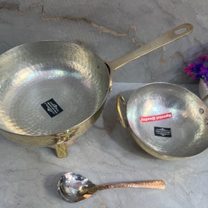 Puede incluir: Dos cuencos de servir de latón martillado con asas, uno con un soporte, y una pequeña cuchara de servir de cobre martillado. Los cuencos tienen una etiqueta que dice "Special Quality".