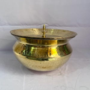 May include: A gold hammered metal pot with a lid. The pot has a rounded body and a small knob on the lid.