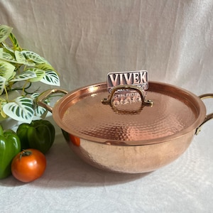 May include: A copper pot with a hammered finish and a brass handle. The pot has a lid with a brass knob and a brass tag that says "Vivek".