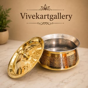 May include: A decorative brass bowl with an oval lid. The bowl has a silver interior and a gold exterior with an embossed floral pattern. The lid is open, revealing the interior. The text "Vivekartgallery" is above the bowl.