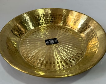 May include: A large, round, hammered brass serving tray with a shiny, golden finish. The tray has a slightly raised rim and a textured surface.