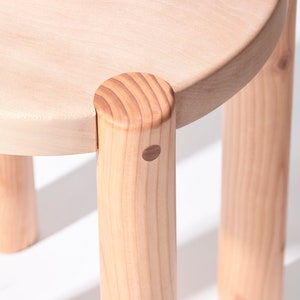 K&ouml;nnte beinhalten: Ein Hocker aus Holz mit einer runden Oberseite und drei Beinen. Der Hocker ist aus hellem Holz gefertigt und hat eine nat&uuml;rliche Oberfl&auml;che.