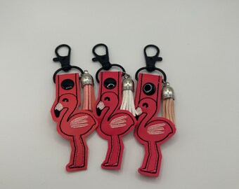 May include: Three pink flamingo keychains with black key rings and silver tassel charms. Each keychain has a different colored tassel.