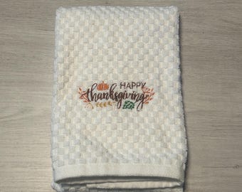 May include: White kitchen towel with a checkered pattern and embroidered text that reads "Happy Thanksgiving" with a small pumpkin design.