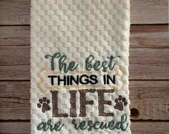 May include: White kitchen towel with green, brown, and yellow embroidery that reads "The best things in life are rescued".