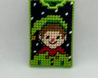 May include: Green and black felt Christmas ornament with a stitched image of an elf with a red hat and a white beard.