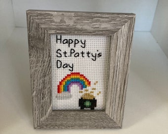 May include: A framed cross-stitch with a rainbow, pot of gold, and the text "Happy St. Patty's Day".