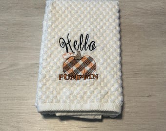 May include: White kitchen towel with embroidered text "Hello Pumpkin" and a brown and white plaid pumpkin.