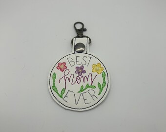 May include: White leather keychain with a round embroidered patch that says "BEST mom EVER" with colorful flowers around the text.