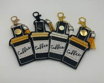 May include: Four black leather keychains with gold and silver accents. Each keychain features a coffee cup design with the word "Coffee" embroidered in black. The keychains have a tassel attached.