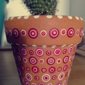 May include: A terracotta flower pot with a white rim and a polka dot pattern in pink and white.