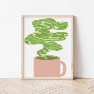 May include: A framed art print featuring a pink mug with green, swirling steam rising from it. The steam has a marbled effect, and the background is white. The frame is a light wood color, and the overall style is minimalist.