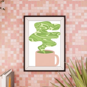 May include: A framed art print featuring a pink mug with green, swirled steam rising from it. The artwork is set against a pink tiled wall, with plants in the foreground and background.