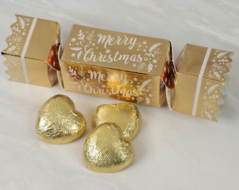 以下が含まれることがあります： 白い花のアクセントと「Merry Christmas」の文字が入った金色のクリスマス・クラッカー。 金色のホイルで包まれたハート型のチョコレートが3つあります。 お祝いの席にぴったりの、お祭り気分を盛り上げるデコレーションです。