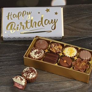 May include: A gold box of assorted chocolates with a white box on top that says "Happy Birthday" in gold lettering.