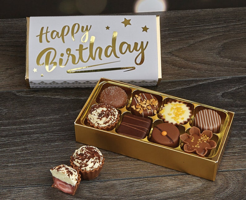 May include: A gold box of assorted chocolates with a white box on top that says "Happy Birthday" in gold lettering.