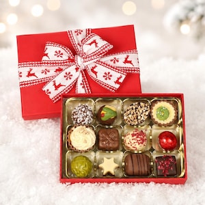 May include: A red gift box with a white ribbon featuring red reindeer and snowflake patterns, containing twelve assorted chocolates in a gold tray. The chocolates include various shapes, textures, and colours like brown, green, red, and white.