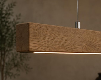 Puede incluir: Una lámpara colgante lineal que presenta una viga rectangular de madera maciza con un patrón de veta natural visible. La lámpara está suspendida por cables metálicos delgados e incluye una tira de luz LED integrada en el borde inferior.