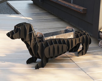 Puede incluir: Hoguera de metal negro con forma de perro salchicha. La hoguera tiene una abertura rectangular para quemar leña.