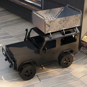 以下が含まれることがあります： 金属製のジープの形をした黒い焚き火台で、上に金属製のグリルが付いています。焚き火台は木製のデッキの上に置かれ、隣には薪の山があります。