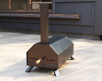 Puede incluir: Un horno de pizza para exteriores de metal negro con una chimenea alta y una base de leña. El horno está sentado en una terraza de madera.