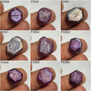 May include: Nine rough-cut gemstones in deep red and purple hues. Each stone has a unique shape and internal crystalline structure, with visible lines and patterns. The gemstones are held in a hand, showcasing their natural beauty. The gemstones are in a hand.