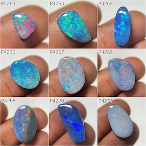 Puede incluir: Nueve piedras preciosas de ópalo pulidas en varias formas y colores. Los ópalos muestran una gama de colores iridiscentes, incluyendo azul, verde, rojo y rosa. Cada piedra se sostiene entre los dedos, mostrando los patrones y tonos únicos.