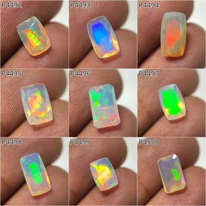 Puede incluir: Una colección de nueve ópalos de corte rectangular, cada uno mostrando un juego de color único. Los ópalos exhiben una variedad de tonos, incluyendo verdes vibrantes, naranjas, azules y amarillos, con destellos internos de iridiscencia. Cada piedra se presenta sobre un fondo neutro.