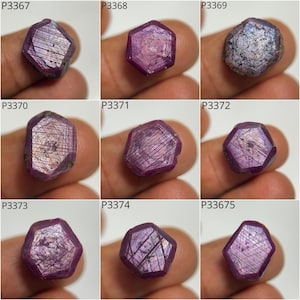 Puede incluir: Nueve piedras preciosas de rubí en bruto, facetadas y de diversas formas. Los rubíes varían en color desde el rosa intenso hasta el rojo púrpura, con estrías internas visibles e inclusiones naturales. Cada piedra se sostiene entre los dedos.