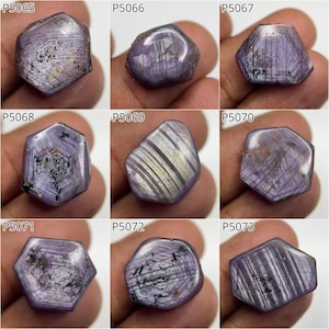 May include: Nine rough-cut, purple gemstones with diverse shapes and surface patterns. Each stone displays a unique internal structure, with visible lines and inclusions. The gemstones are presented against a neutral backdrop, emphasizing their natural colours and textures.