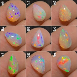 Può includere: Nove opali a forma di goccia con giochi di colore iridescenti. Ogni gemma mostra un motivo unico di colori interni, tra cui blu, verdi, arancioni e viola, su una base bianco latte o traslucida. Gli opali variano per dimensioni e forma.