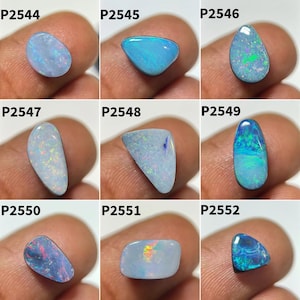 May include: Nine polished opal gemstones in various shapes and colours, including blue, white, and iridescent hues. Each stone is held between fingers, showcasing the unique patterns and textures of the opals. The gemstones are labelled with individual product codes.