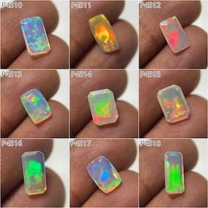 Puede incluir: Una colección de nueve piedras preciosas de ópalo rectangulares, cada una con un juego de color único. Los ópalos exhiben una gama de tonos, incluyendo azules, verdes, naranjas y rojos. Cada piedra se sostiene contra un fondo color piel.