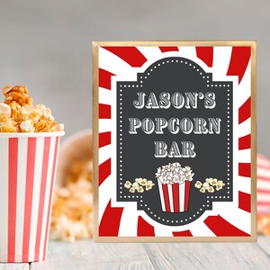 May include: A red and white striped sign with a black chalkboard insert that says "Jason's Popcorn Bar". The sign is framed in gold and has a red and white striped background.