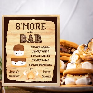 Pode incluir: Uma placa de madeira com fundo marrom e moldura dourada que diz "S'more Bar" com uma ilustração fofa de um s'more. A placa lista "S'more Laugh, S'more Hugs, S'more Kisses, S'more Love, S'more Memories". A placa também diz "Jason's Birthday" e "Party S'more".