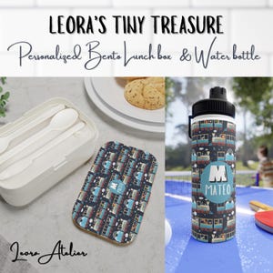 Puede incluir: Una fiambrera bento blanca con un patrón de tren azul y rojo en la tapa. La fiambrera viene con un juego de tres cucharas. Una botella de agua azul con un patrón de tren y el nombre "Mateo" en ella.