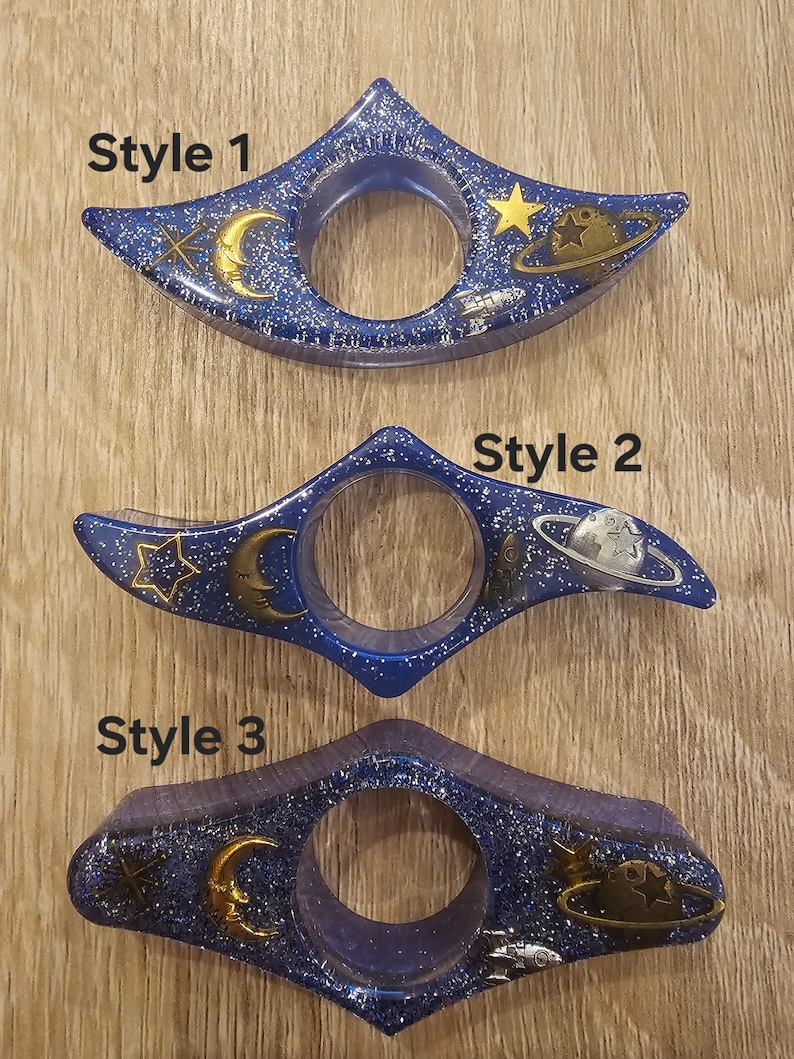 K&ouml;nnte beinhalten: Drei Lesezeichen in Blau und Silberglitter mit Weltraumthema. Jedes Lesezeichen zeigt einen Halbmond, einen Stern, eine Rakete und einen Planeten mit Ringen. Die Lesezeichen sind mit "Style 1", "Style 2" und "Style 3" beschriftet.